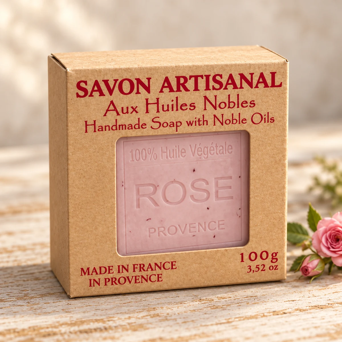 Maître Savonitto Seife Rose in vollständig sichtbarer Kraftkartonverpackung mit Sichtfenster, neben einer rosa Rose auf hellem Holz.
