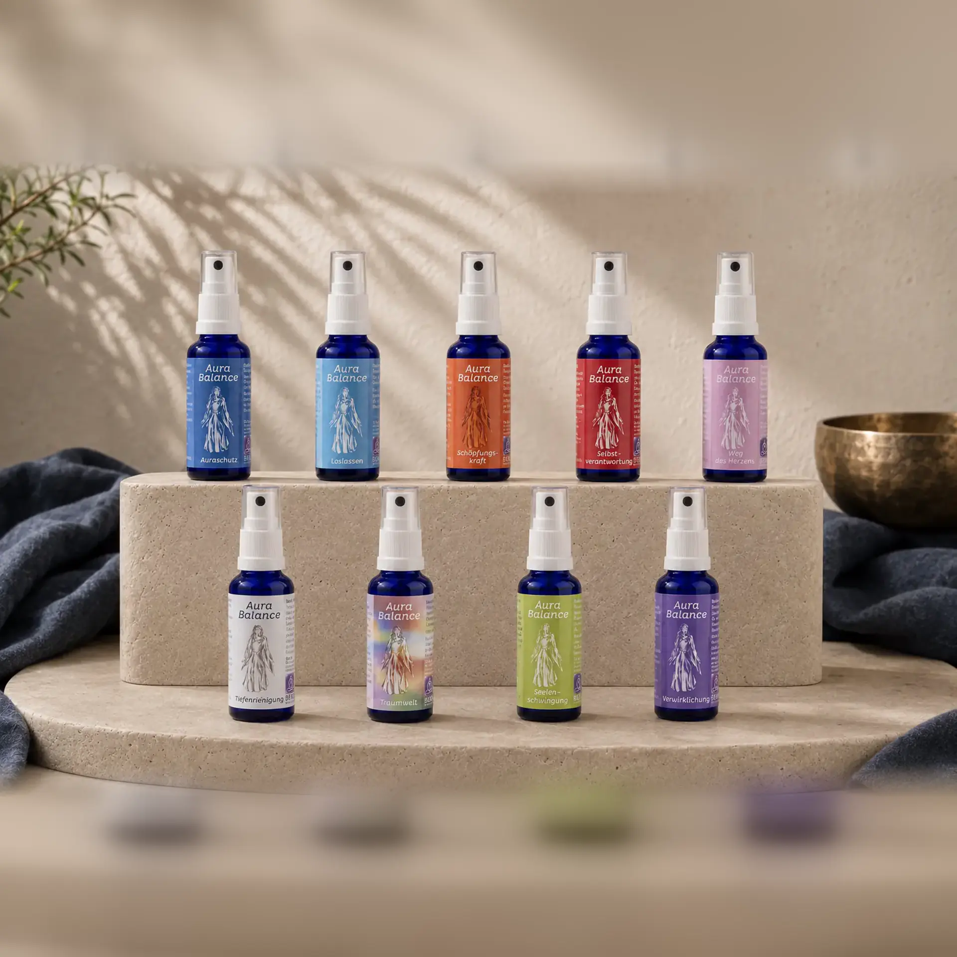 Neun Aura-Balance-Sprays von Berk auf hellen Travertinpodesten mit Klangschale.