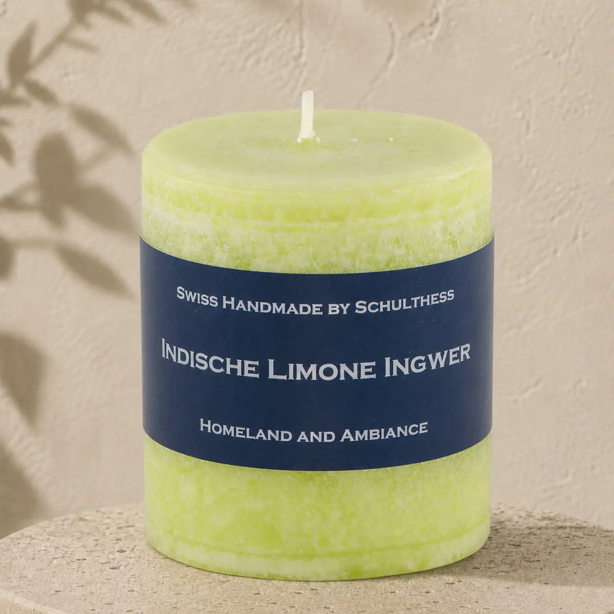 Limonengrüne Schulthess Duftkerze Indische Limone Ingwer auf einem runden Travertinsockel vor einer hellen, strukturierten Wand.