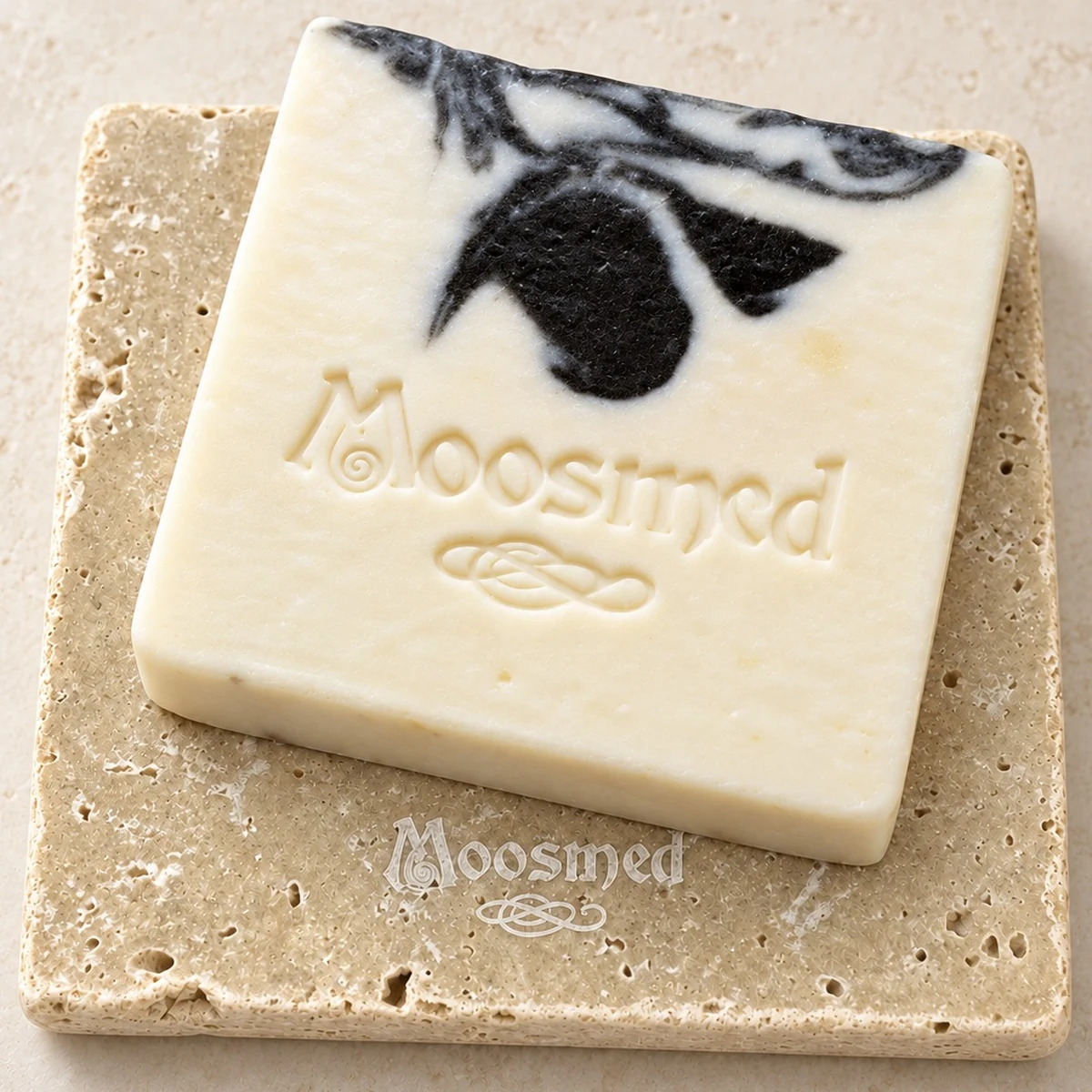 Cremefarbene Moosmed-Männersache-Seife mit schwarzer Marmorierung und geprägtem Logo auf einem quadratischen Travertinteller.