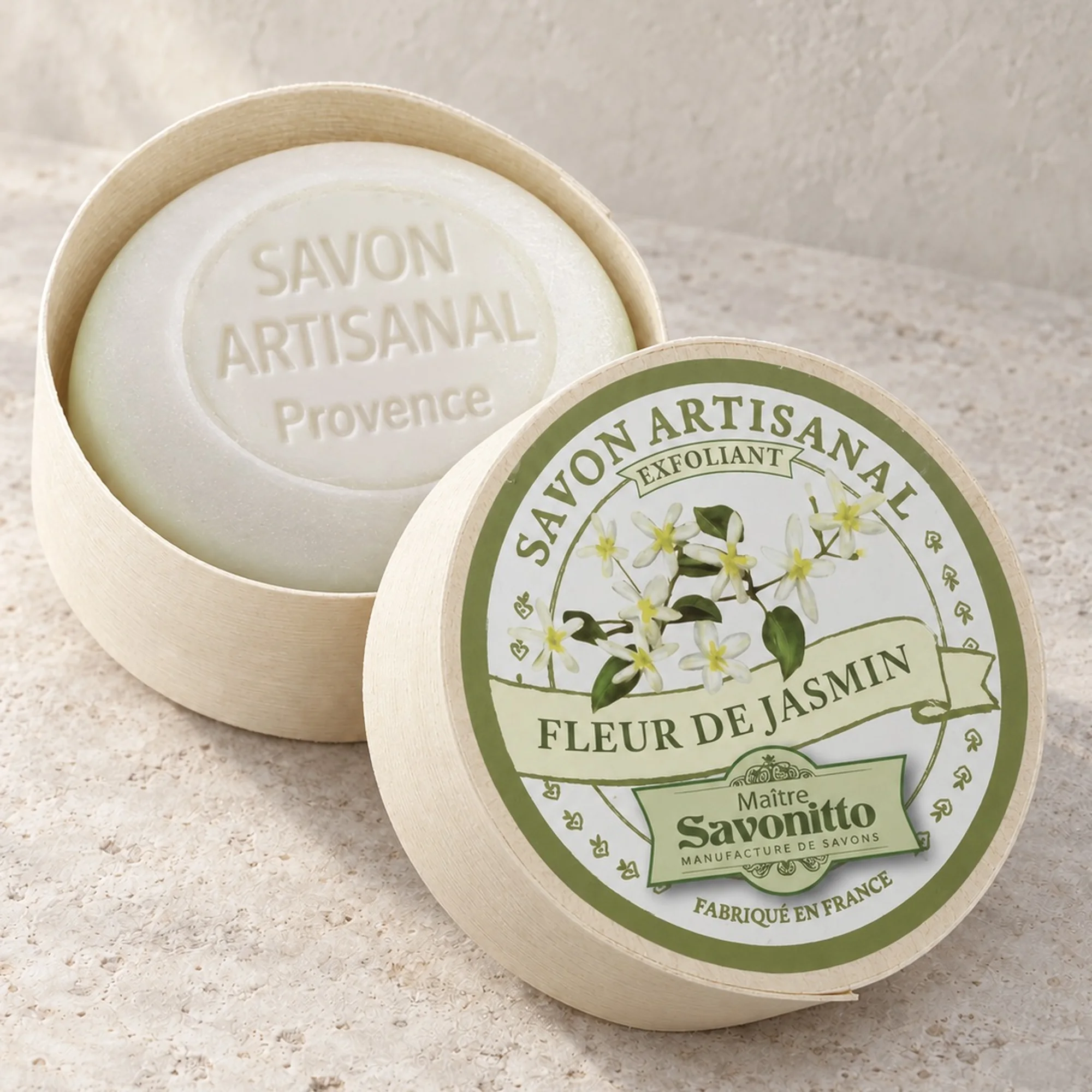 Maître Savonitto Jasmin in offener runder Holzschachtel mit angelehntem Etikettdeckel auf heller Steinfläche.