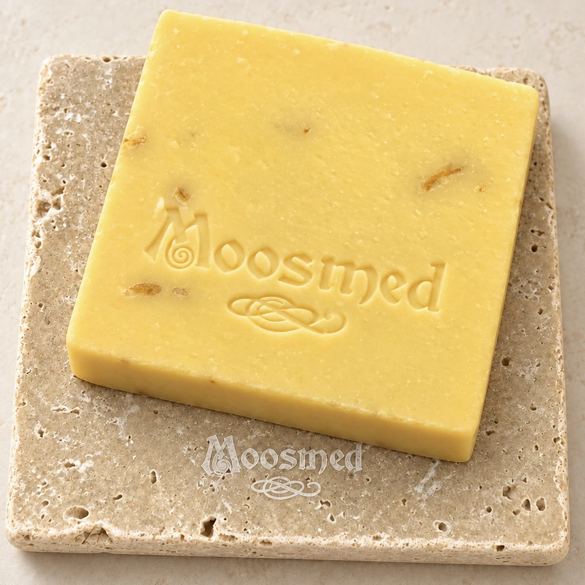 Goldgelbe Moosmed-Calendula-Seife mit Blütenstückchen und geprägtem Logo auf einem quadratischen Travertinteller.