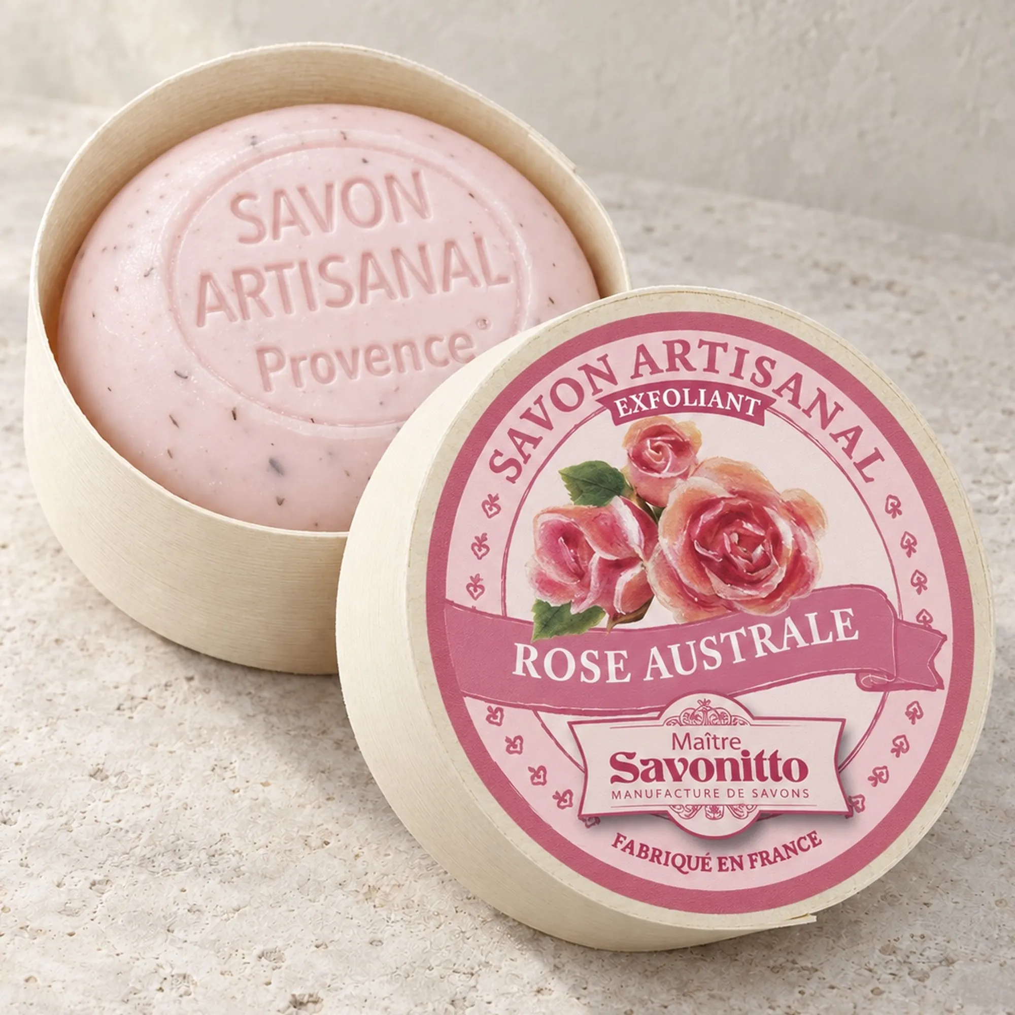 Maître Savonitto Rose Australe in offener runder Holzschachtel mit angelehntem Etikettdeckel auf heller Steinfläche.