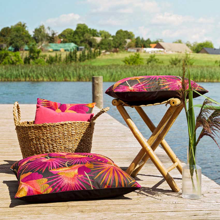 Magma Kissen „Sumatra“ mit tropischem Muster in kräftigem Pink, Orange und Rot auf dunklem Grund – sommerliche Dekoration im Outdoor-Bereich am Wasser.