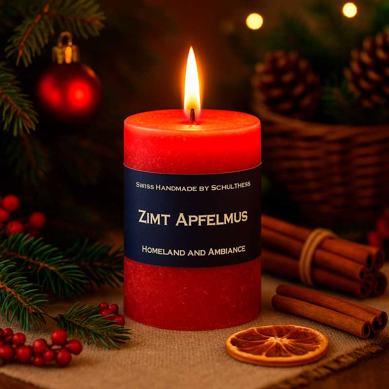 Brennende rote Duftkerze mit der Aufschrift „Zimt Apfelmus – Swiss Handmade by Schulthess“. Umgeben von Tannenzweigen, Zimtstangen, getrockneten Orangenscheiben und weihnachtlicher Dekoration.