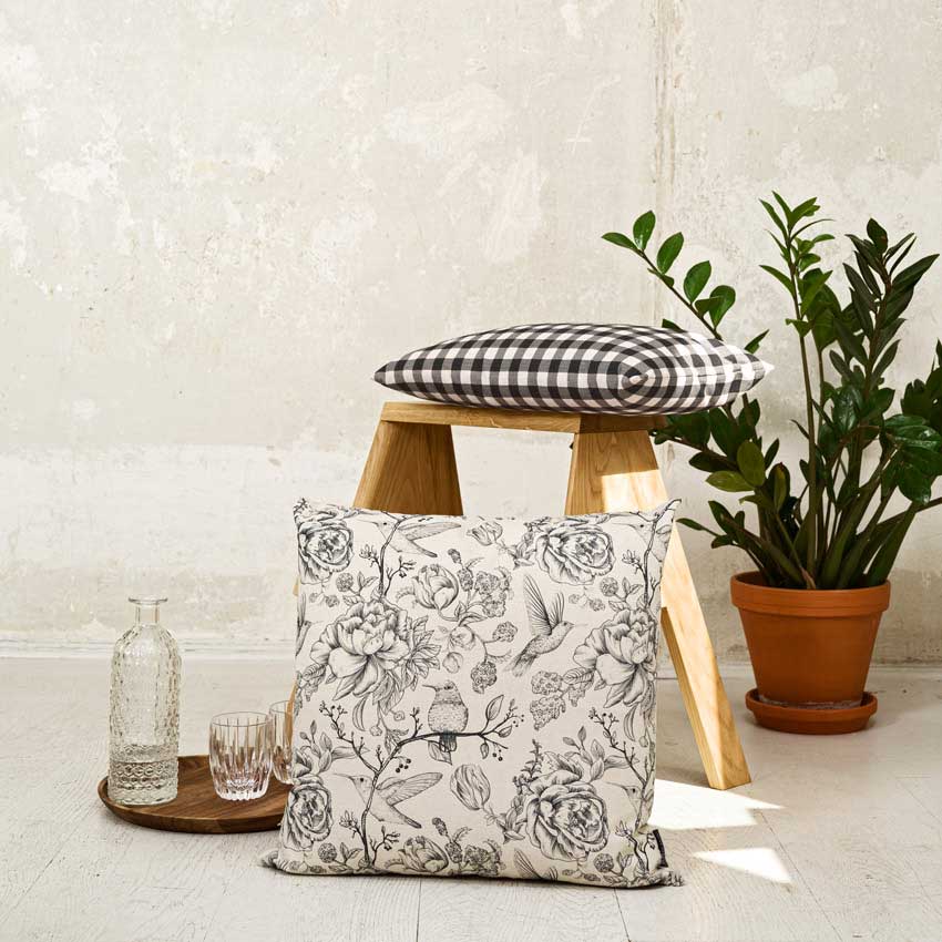 Magma Kissenserie „Cabane“ mit klassischem Landhaus-Charme – florale und karierte Designs in Schwarz-Weiß, kombiniert mit natürlichen Materialien und Pflanzen.