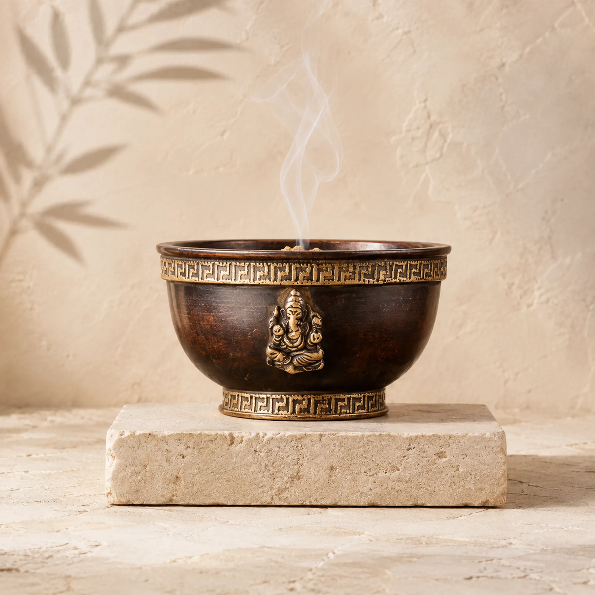 Dunkle Berk Räucherschale in Bronzeoptik mit Ganesha-Relief, Mäanderbordüren und feinem Rauch auf hellem Naturstein