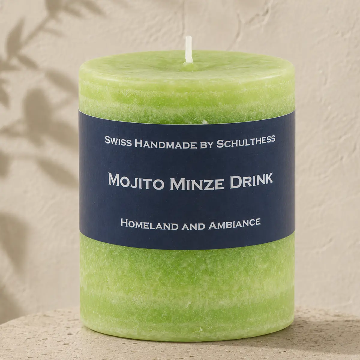 Hellgrüne Schulthess Duftkerze Mojito Minze Drink auf einem runden Travertinsockel vor einer hellen, strukturierten Wand.