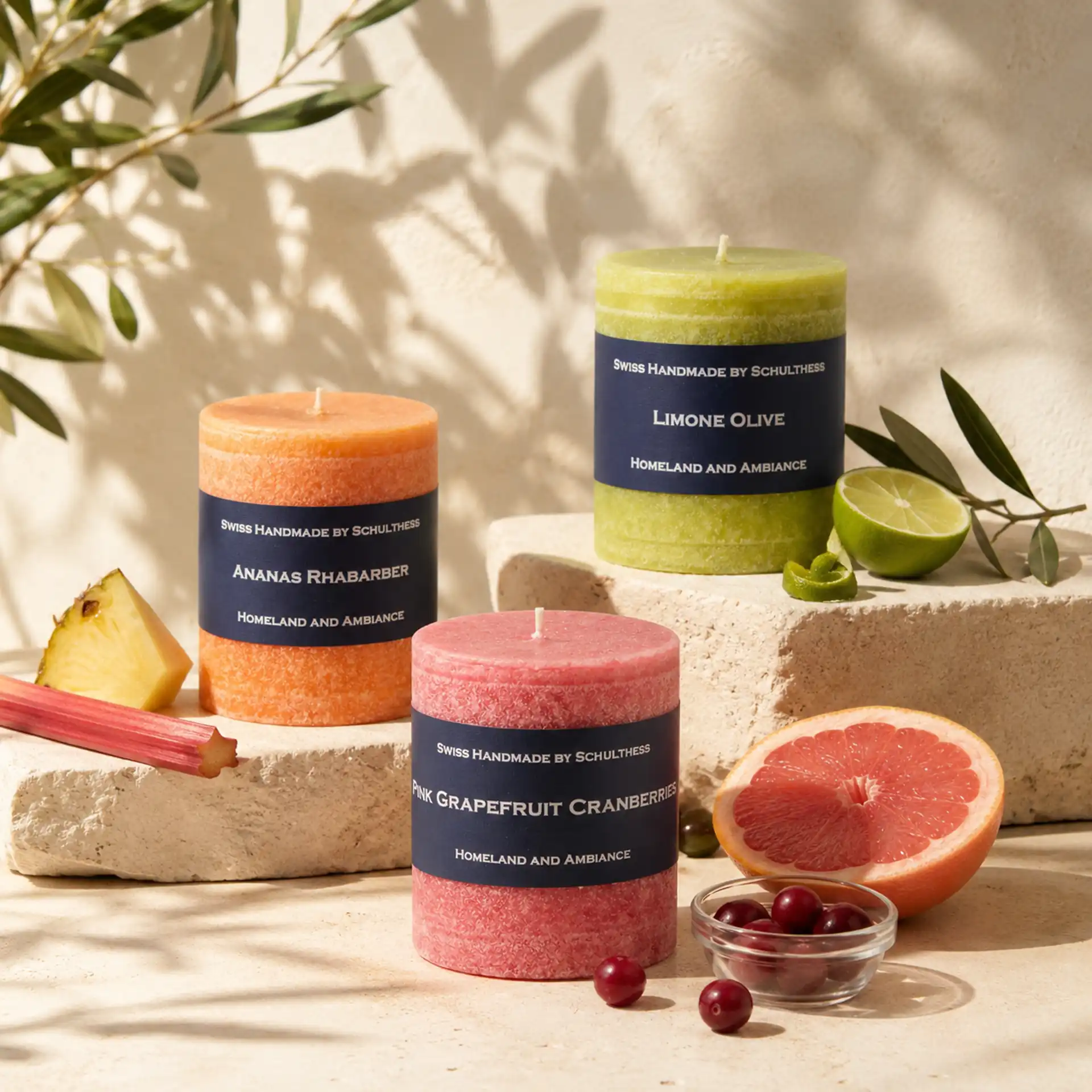 Schulthess Duftkerzen Ananas Rhabarber, Limone Olive und Pink Grapefruit Cranberries mit frischen Früchten auf Natursteinpodesten