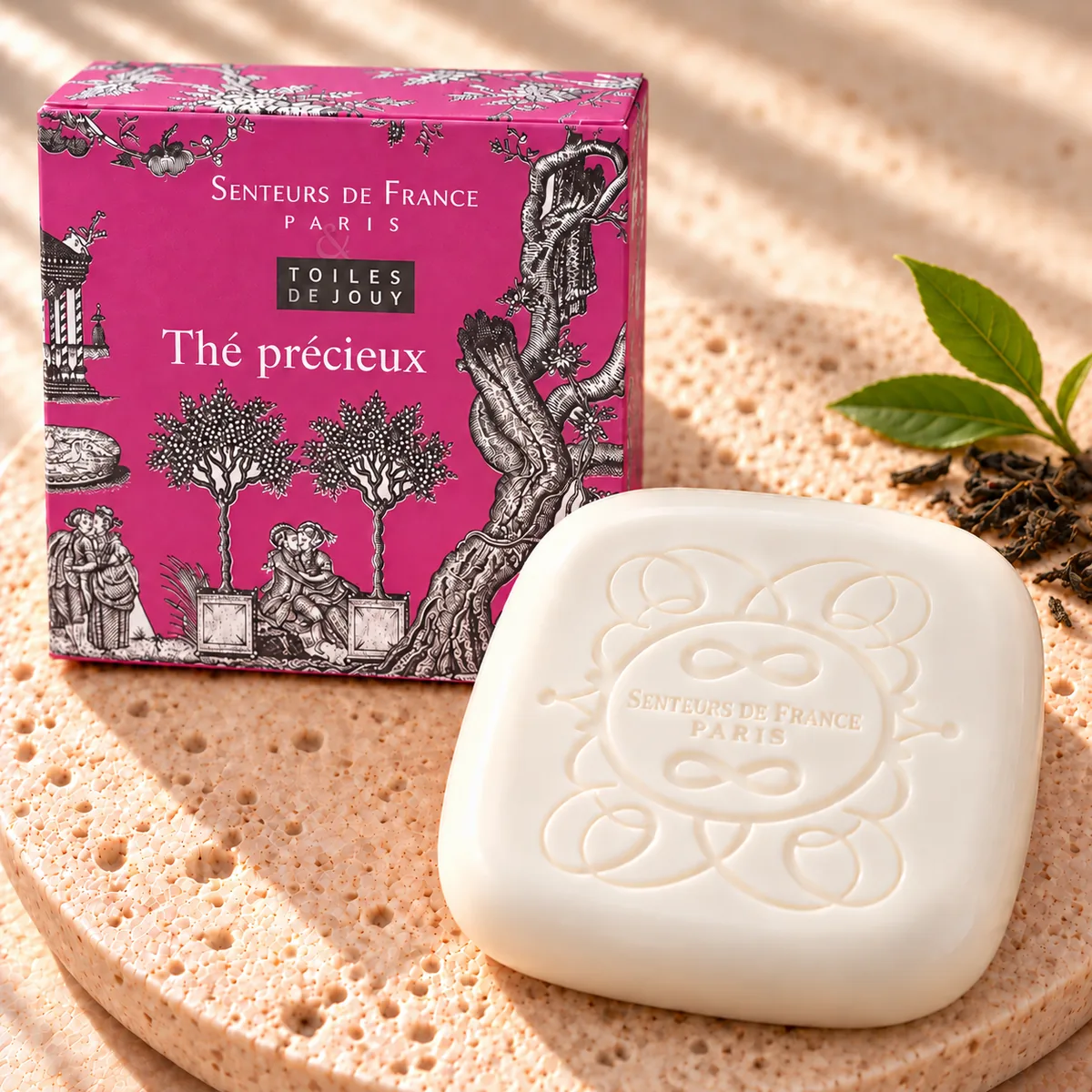 Cremefarbene Thé-Précieux-Seife von Senteurs de France auf Travertin mit pinkfarbener Toile-de-Jouy-Schachtel und rosa Beeren.