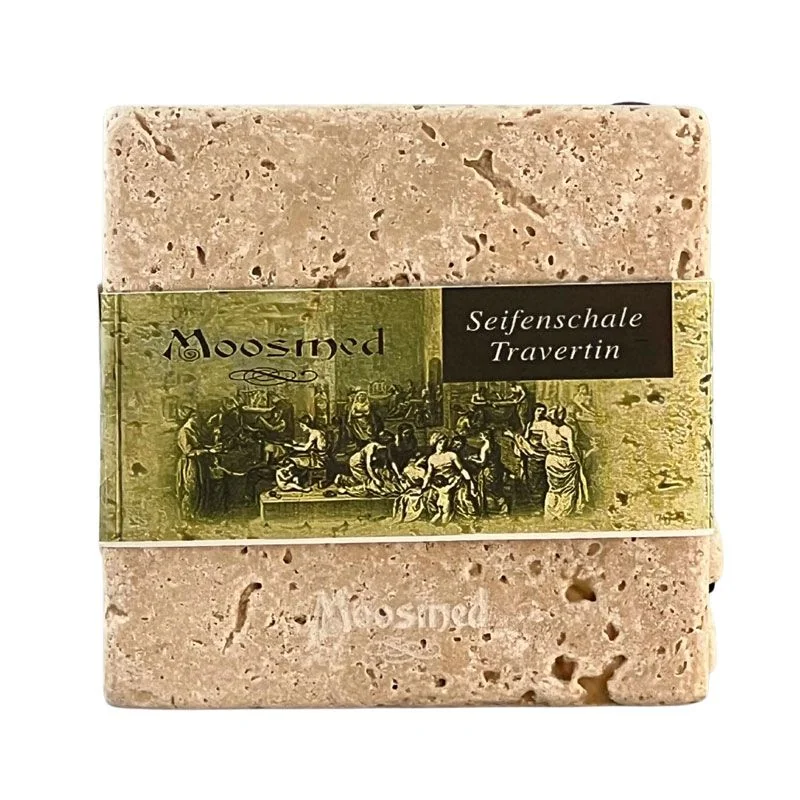Quadratische Moosmed-Seifenschale aus beigem Travertin mit natürlicher Porenstruktur, abgerundeten Ecken und grüner Papierbanderole auf weißem Hintergrund.