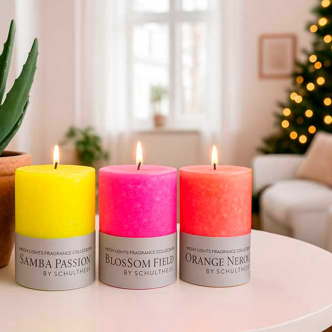 Drei brennende Duftkerzen der Neon Lights Fragrance Collection von Schulthess in leuchtendem Gelb, Pink und Orange mit den Düften Samba Passion, Blossom Field und Orange Neroli. Im Hintergrund ein helles Wohnzimmer mit Weihnachtsbaum.