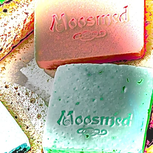 Künstlerisch verfremdete Nahaufnahme geprägter Moosmed-Seifen in Rosa und Türkis auf Travertin.