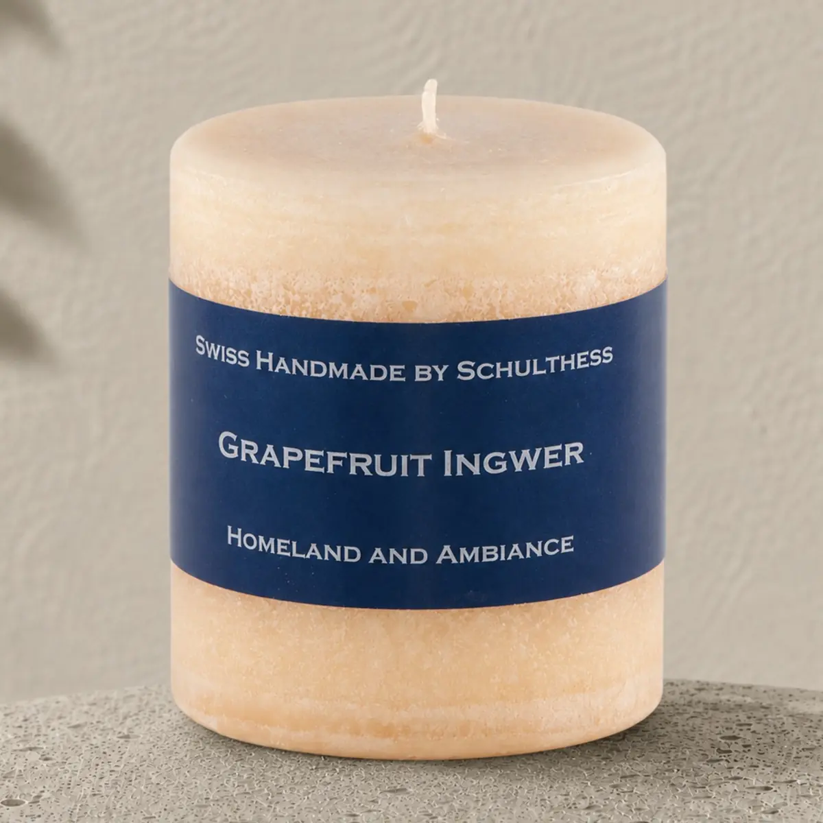 Apricotfarbene Schulthess Duftkerze Grapefruit Ingwer auf hellem Travertin vor einer warmen, strukturierten Wand.