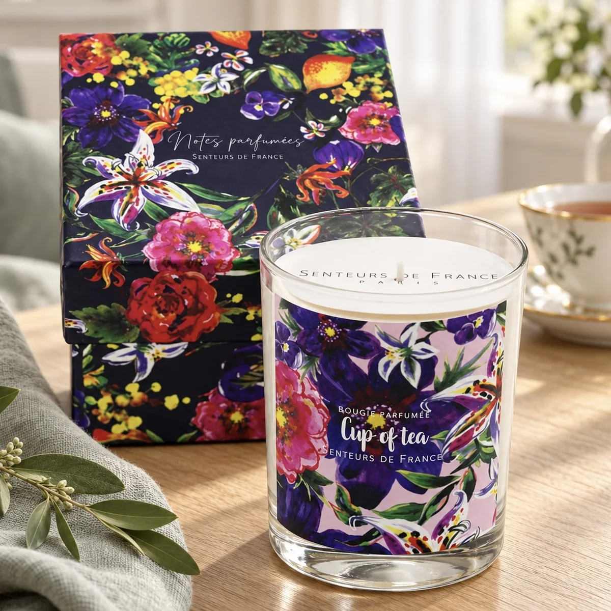 Duftkerze Cup of Tea von Senteurs de France mit floraler Geschenkbox, Teetasse und salbeifarbenem Leinen auf Holz.