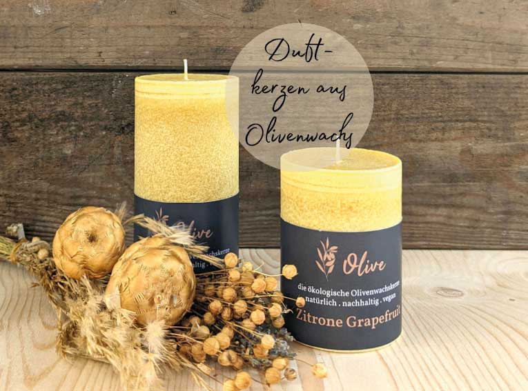 Zwei gelbe Duftkerzen aus Olivenwachs mit der Aufschrift „Zitrone Grapefruit“ stehen auf einem Holztisch vor rustikalem Hintergrund. Daneben liegen getrocknete Blumen und Pflanzendekoration.