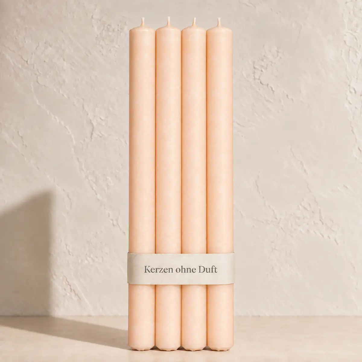 Vier Schulthess Stabkerzen in Apricot hell mit beiger Banderole „Kerzen ohne Duft“ vor einer hellen, warmen Wand.
