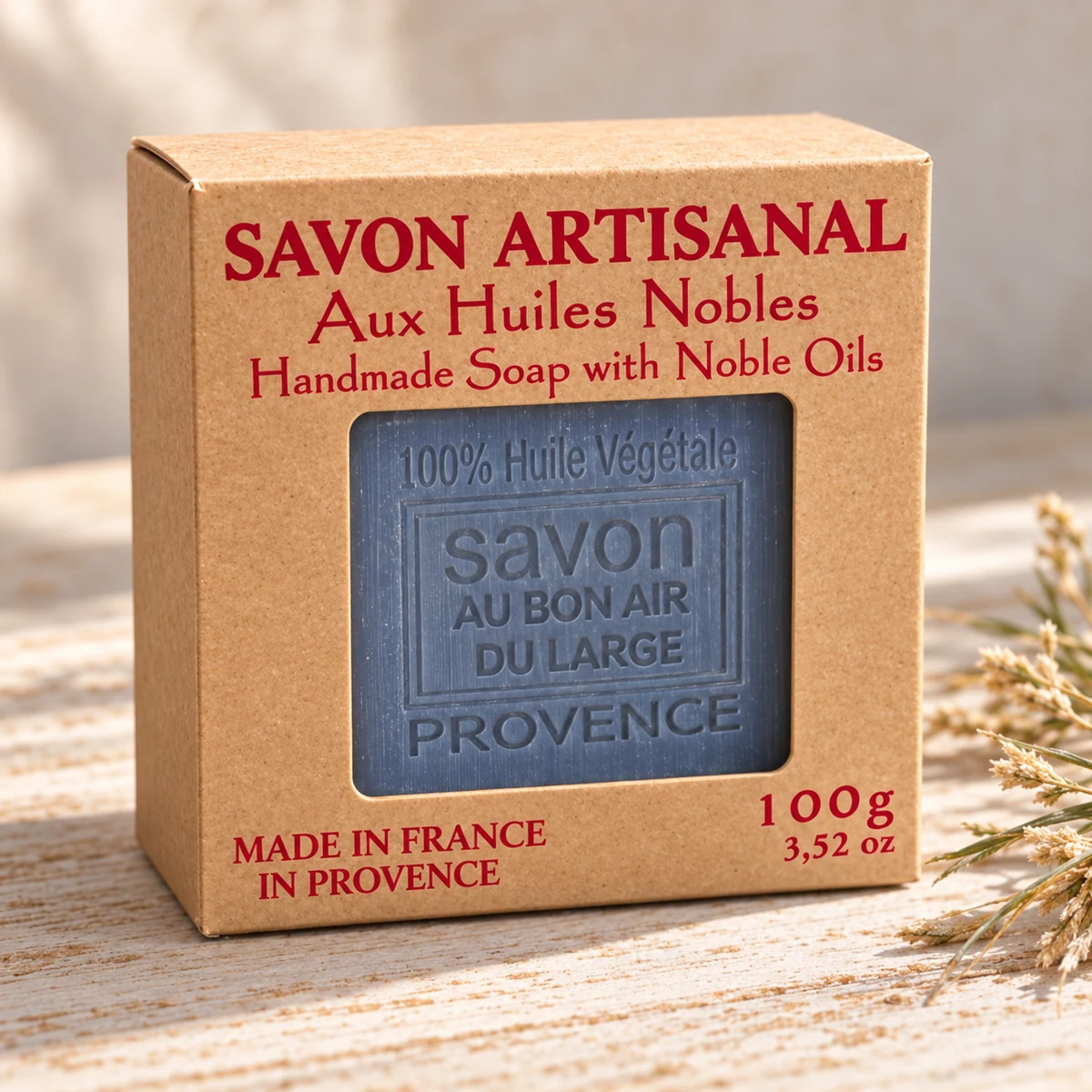 Maître Savonitto Seife Air du Large in vollständig sichtbarer Kraftkartonverpackung mit Sichtfenster, neben dezenten Gräsern auf hellem Holz.