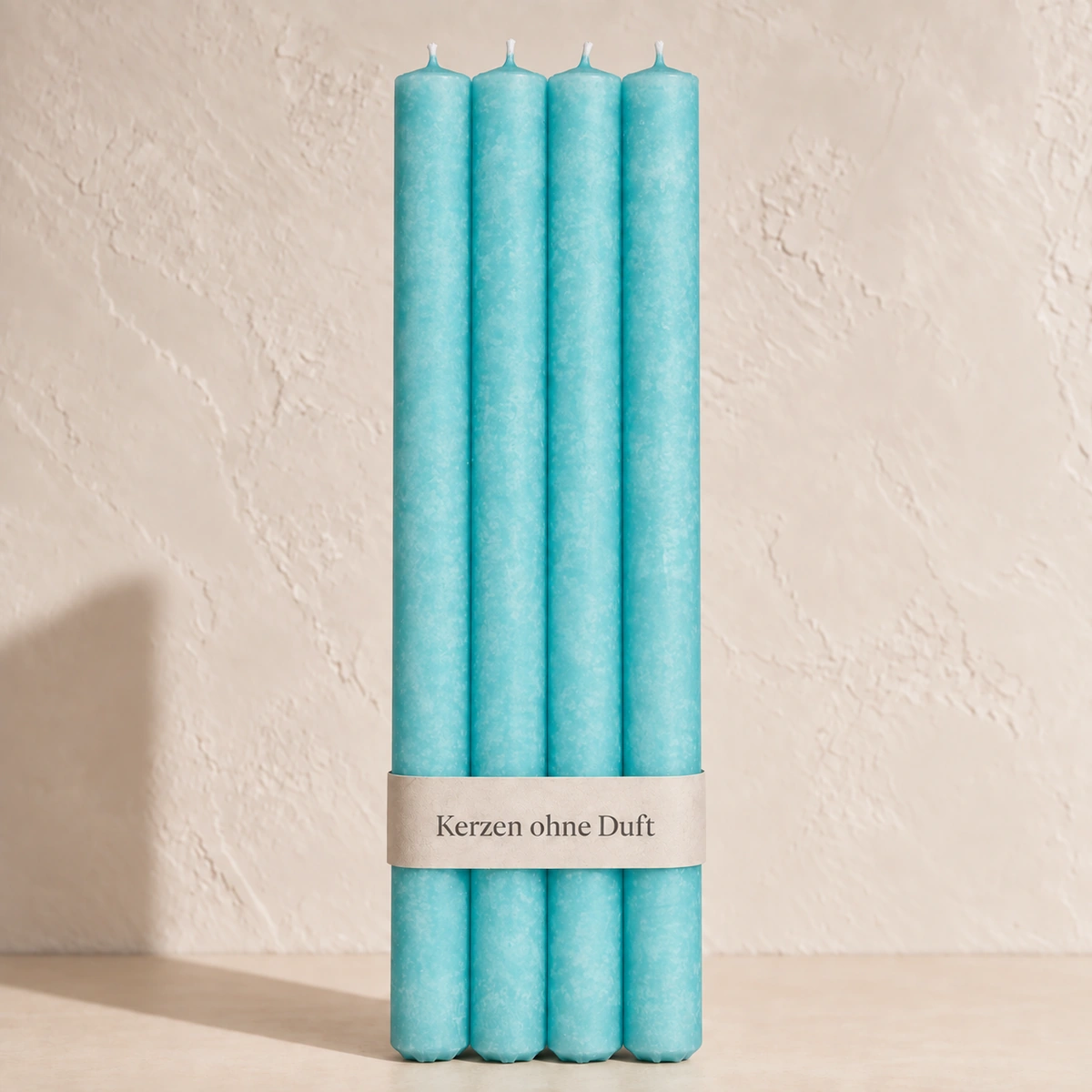 Vier Schulthess Stabkerzen in Placid Blue mit beiger Banderole „Kerzen ohne Duft“ vor einer hellen, warmen Wand.