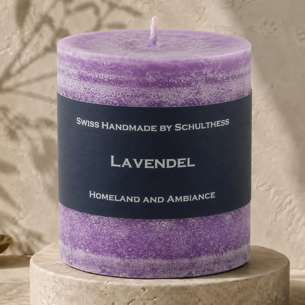 Violette Schulthess Duftkerze Lavendel auf einem runden Travertinsockel vor einer hellen, strukturierten Wand.