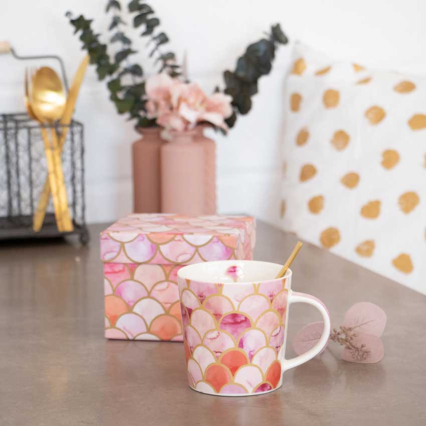 Art-Déco-Porzellantasse von PPD mit rosa, gold- und pfirsichfarbenem Schuppenmuster, dekorativ auf modernem Tisch mit Geschenkbox und goldenem Löffel arrangiert.