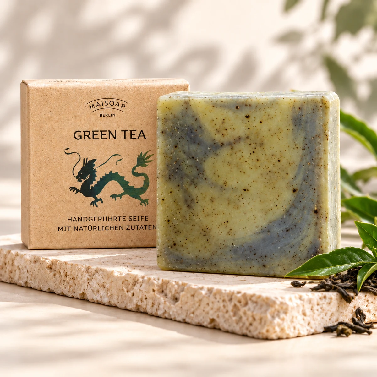 Gesprenkelte Maisoap Green-Tea-Seife mit Verpackung und Teeblättern auf heller Steinplatte