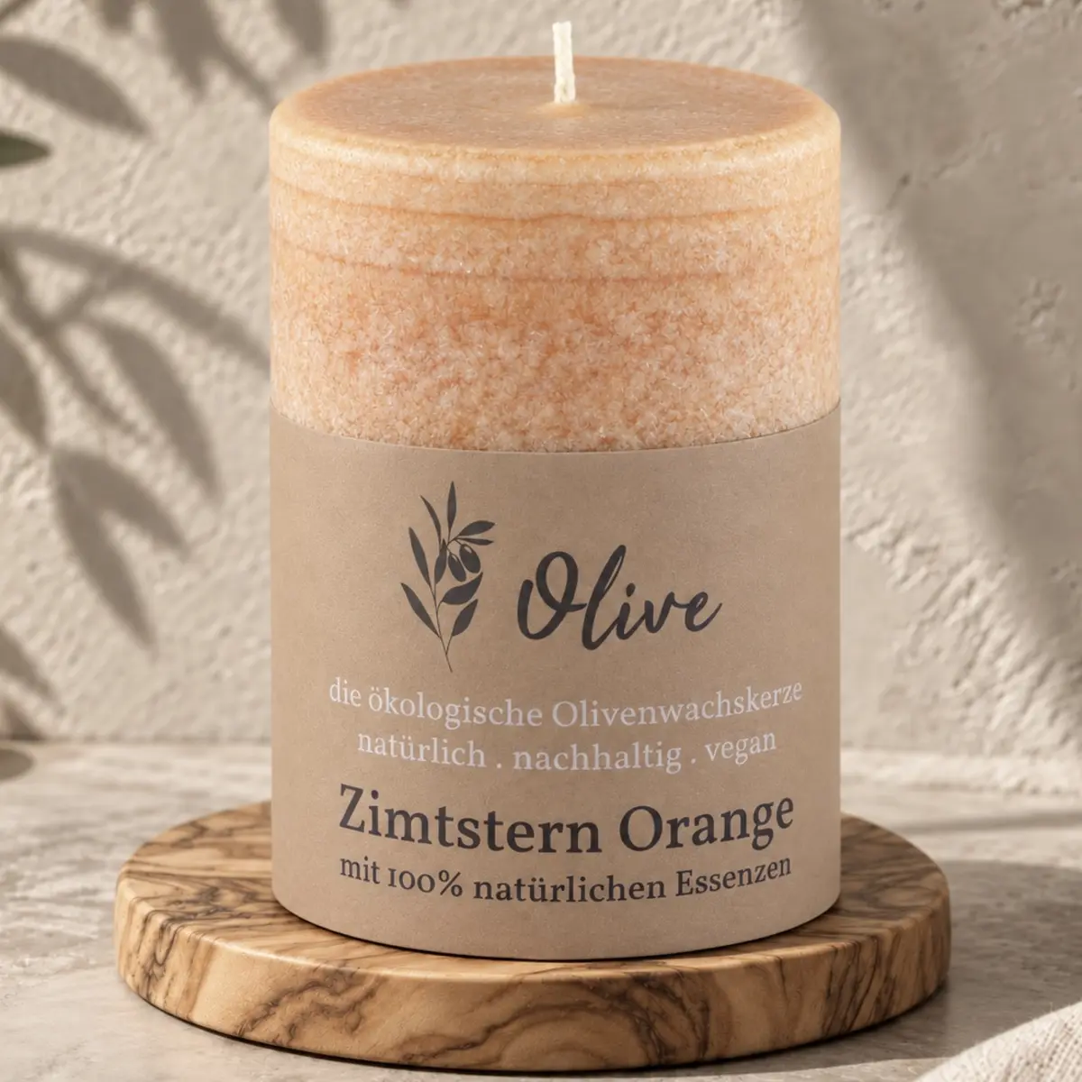 Schulthess Olivenwachskerze Zimtstern Orange auf einem runden Holzteller