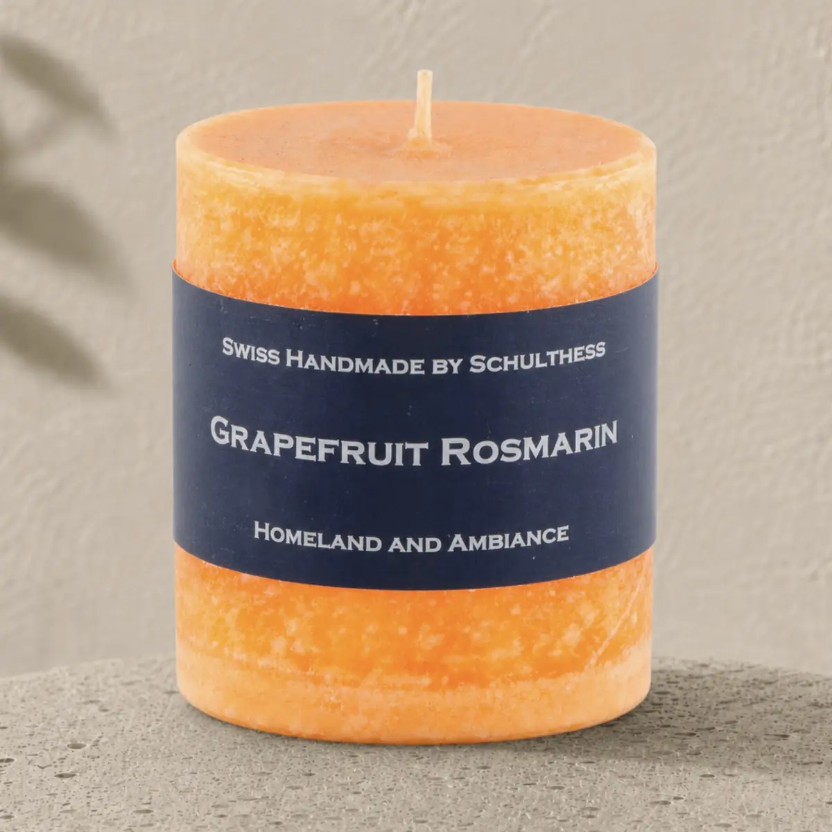 Orangefarbene Schulthess Duftkerze Grapefruit Rosmarin auf hellem Travertin vor einer warmen, strukturierten Wand.