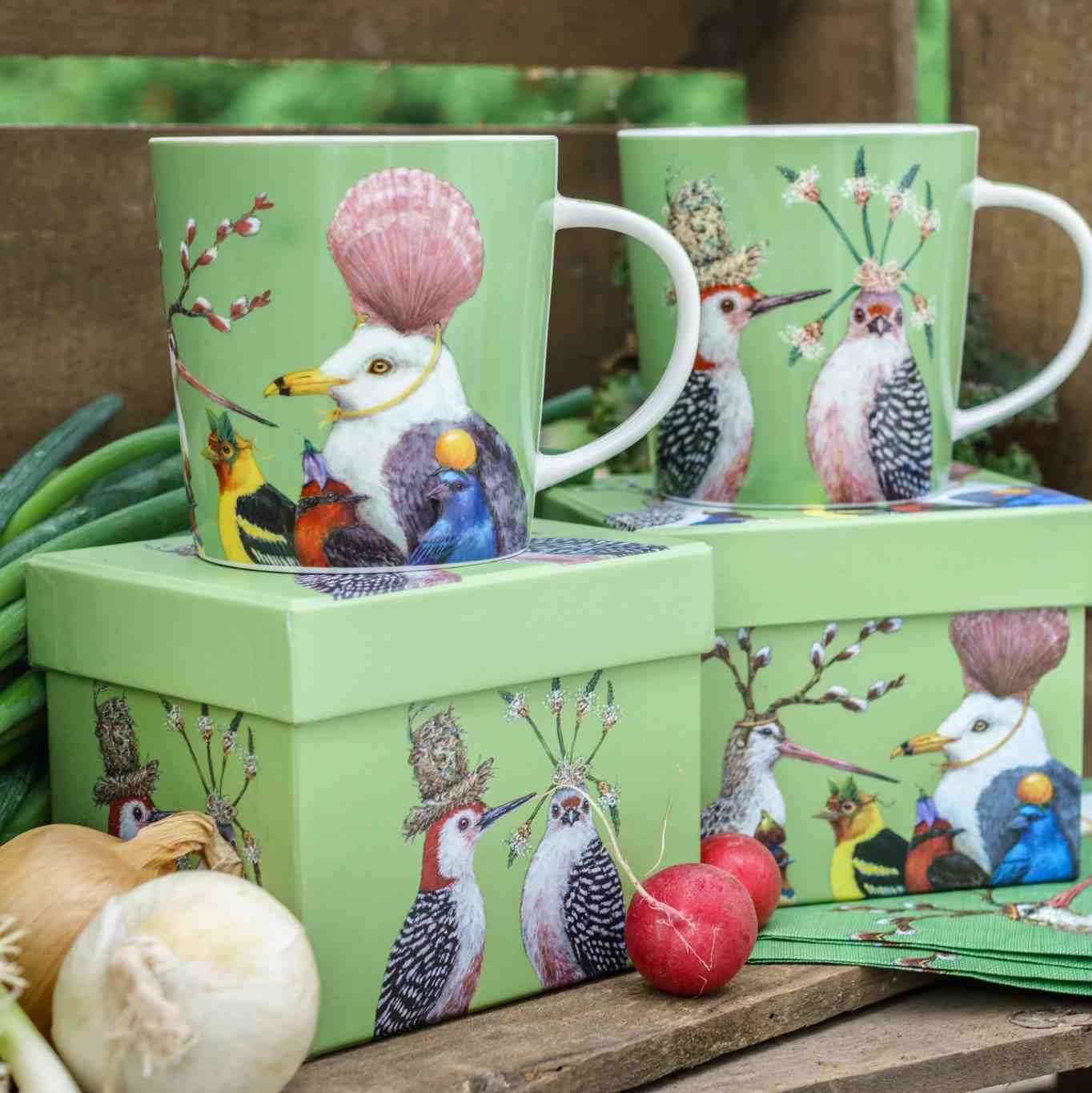 Porzellantasse Sully’s Party von PPD in frischem Grün mit fantasievollen Vogelmotiven. Präsentiert mit passender Geschenkbox, Radieschen und Frühlingsdeko auf rustikalem Holztisch.