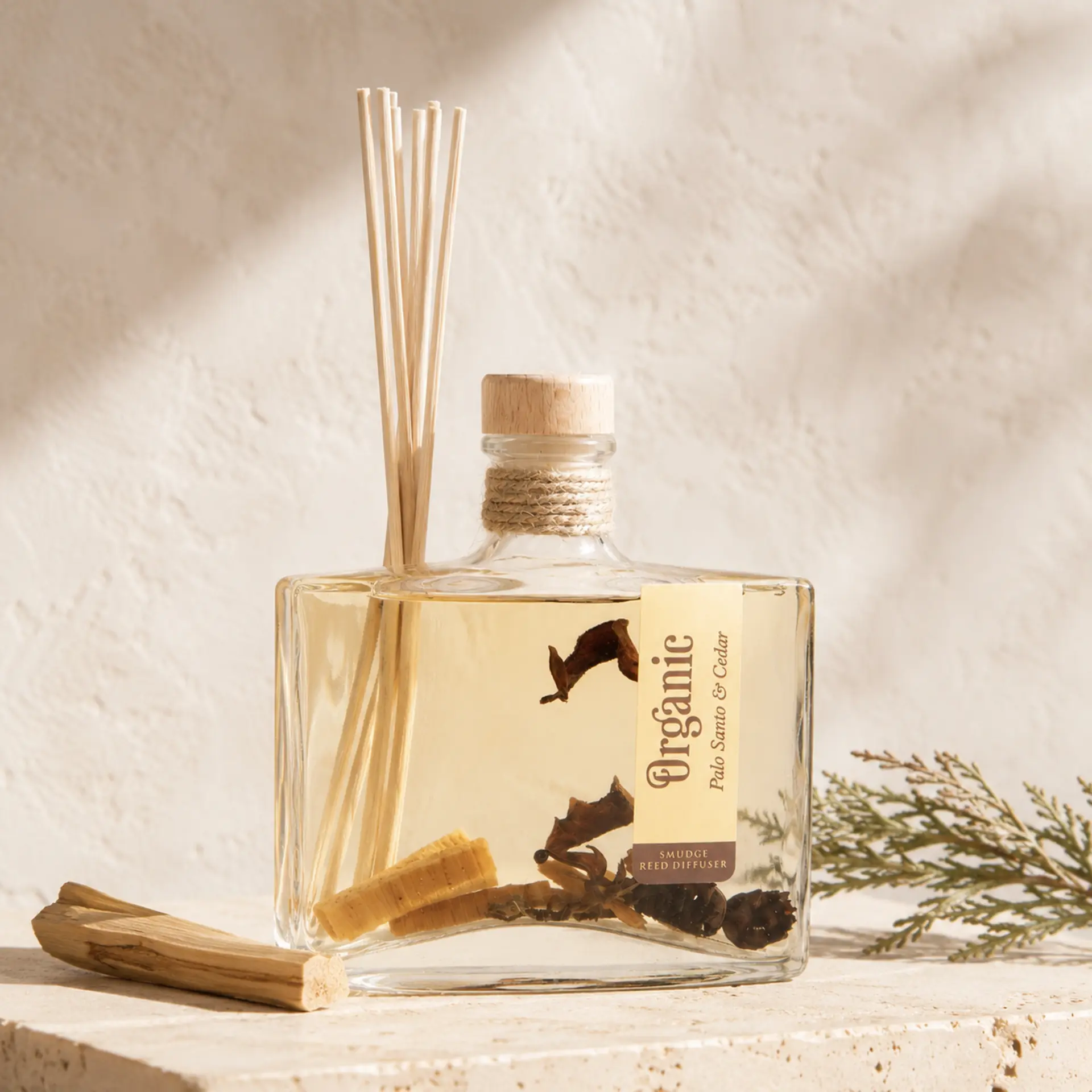 Organic Goodness Reed Diffuser Palo Santo & Cedar mit Holzstück und Zedernzweig auf hellem Travertin.