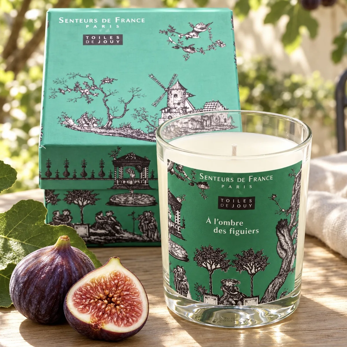 Duftkerze À l’ombre des figuiers von Senteurs de France mit grüner Toile-de-Jouy-Geschenkbox, Feigen und Feigenblättern auf Holz.