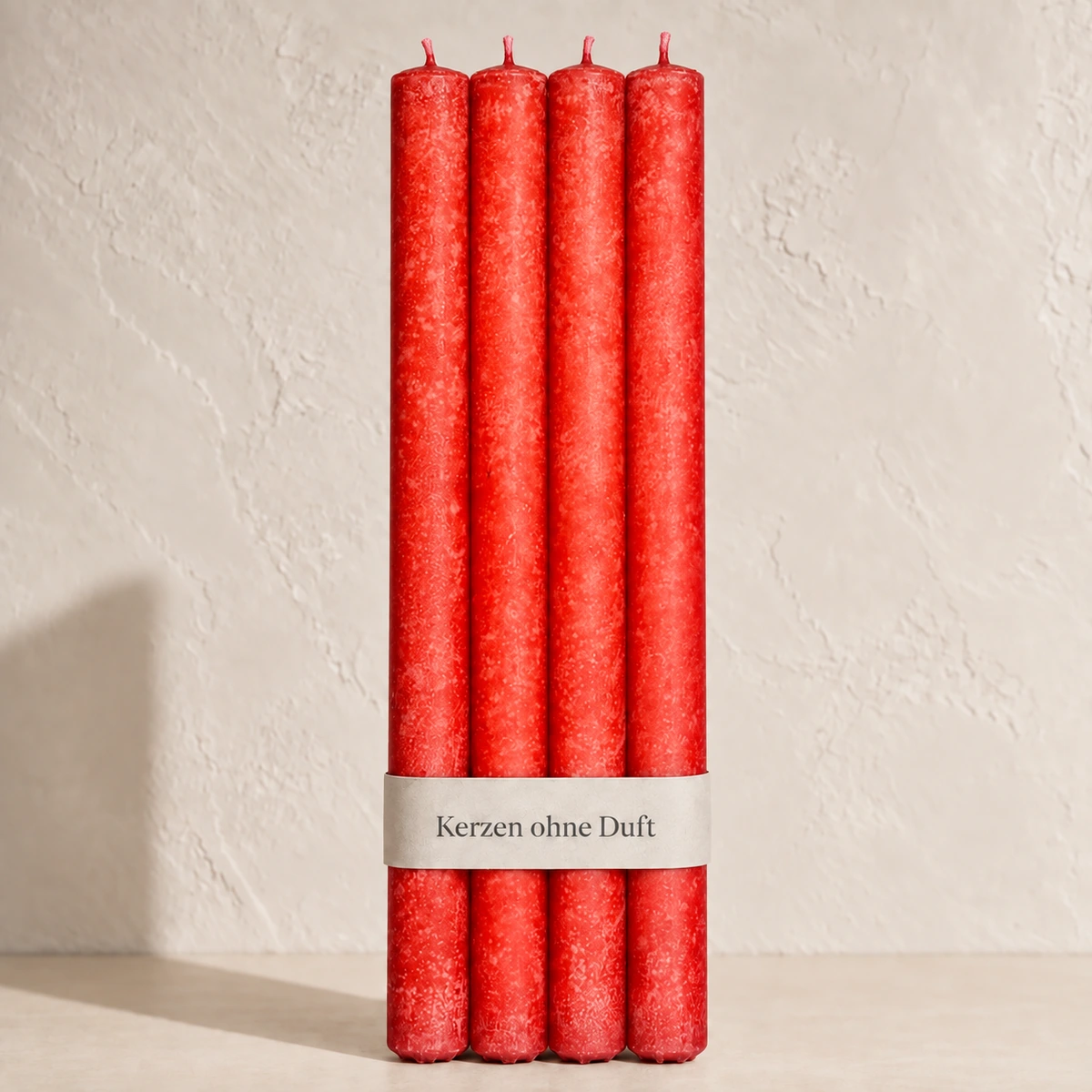Vier Schulthess Stabkerzen in Tangerine mit beiger Banderole „Kerzen ohne Duft“ vor einer hellen, warmen Wand.