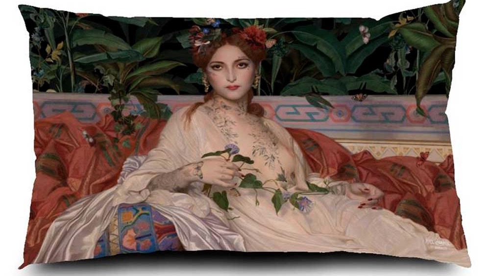 Voglio Bene Samtkissen Albaydé 40x65 – kunstvolles Porträt einer liegenden Frau in cremefarbener Gewandung, mit Tattoos, Blumenkranz und Blätterranke in der Hand, auf opulentem Sofa vor exotischer Pflanzenkulisse.