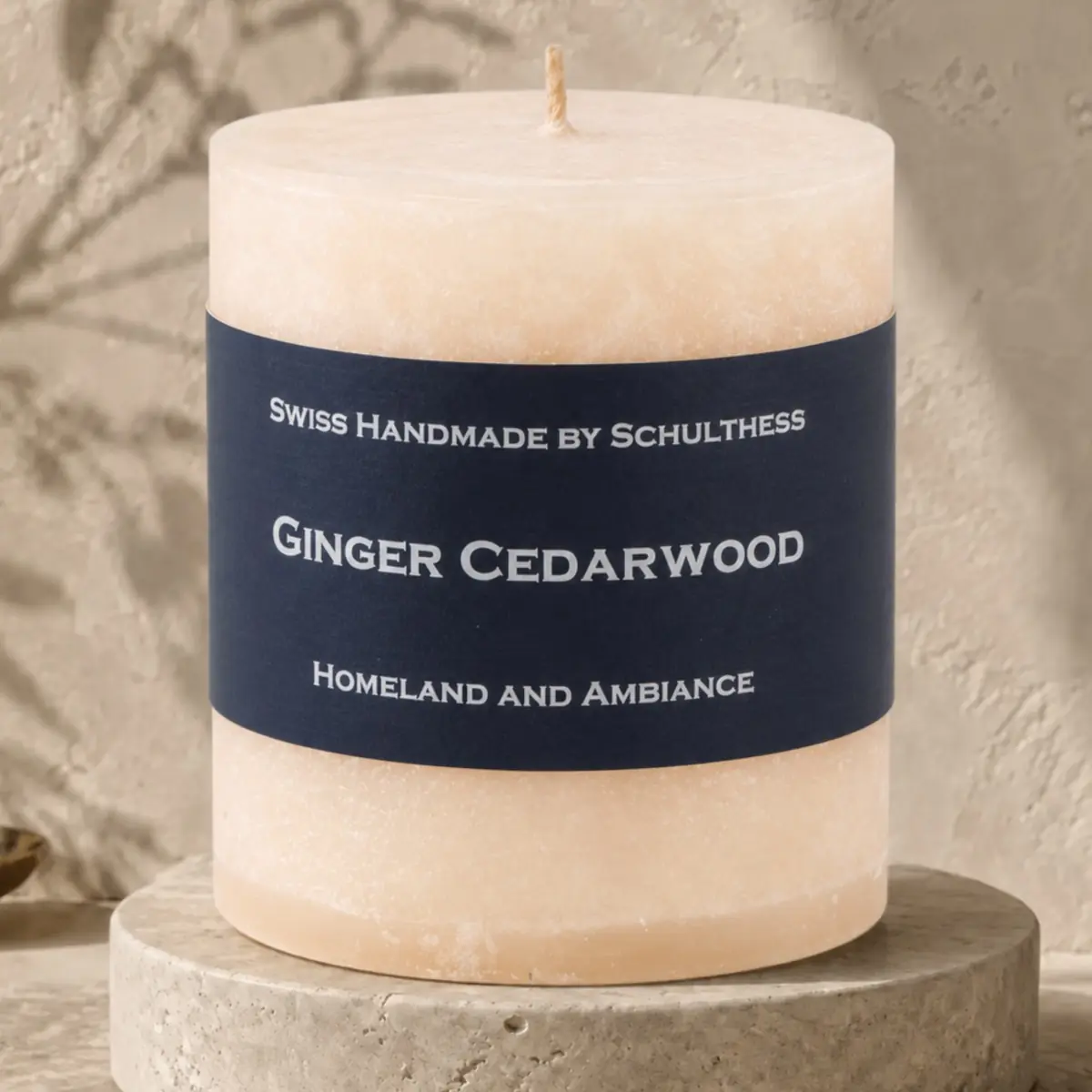 Beige Schulthess Duftkerze Ginger Cedarwood auf einem runden Travertinsockel vor einer hellen, strukturierten Wand.