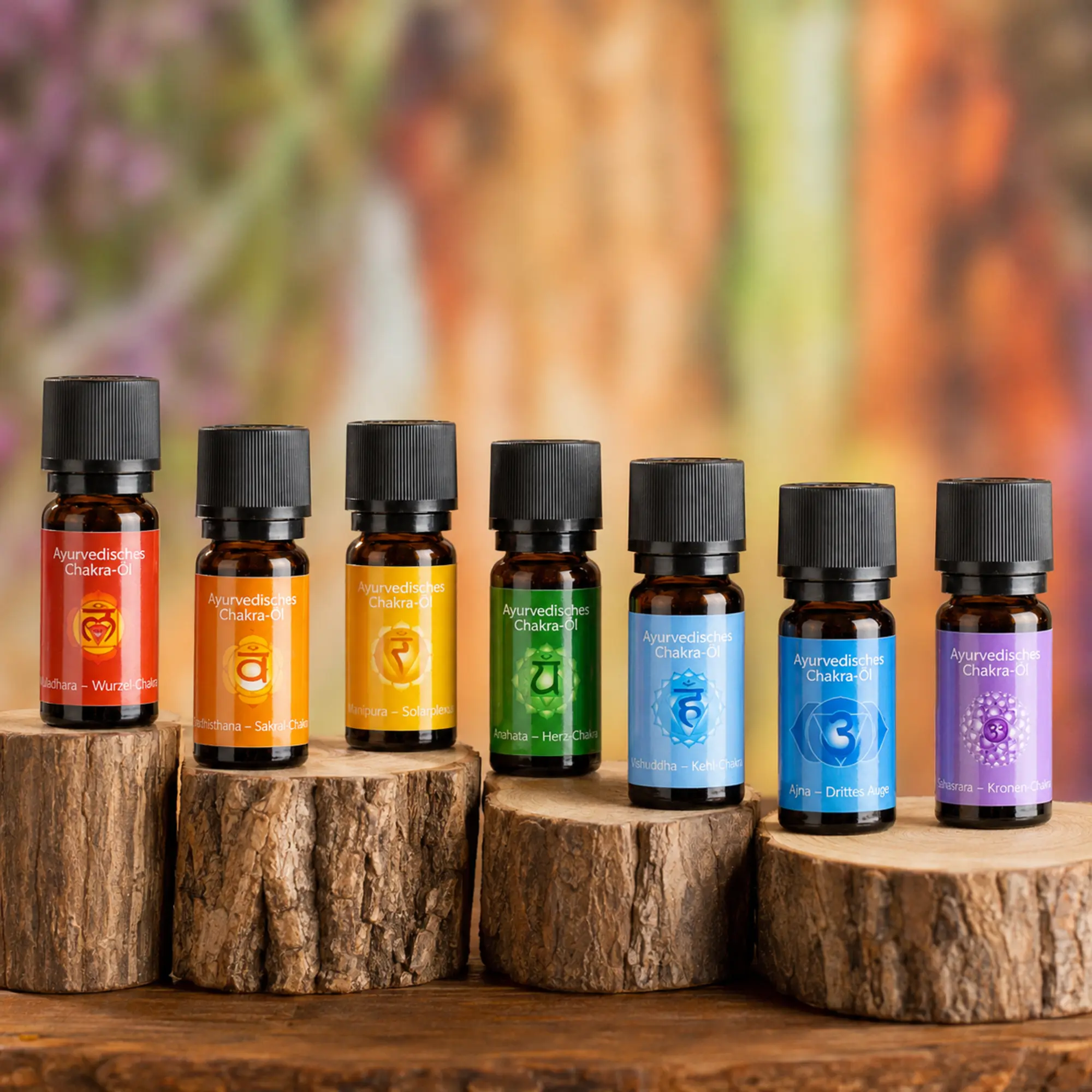 Sieben ayurvedische Chakra-Öle von Berk in den Chakra-Farben auf natürlichen Holzpodesten