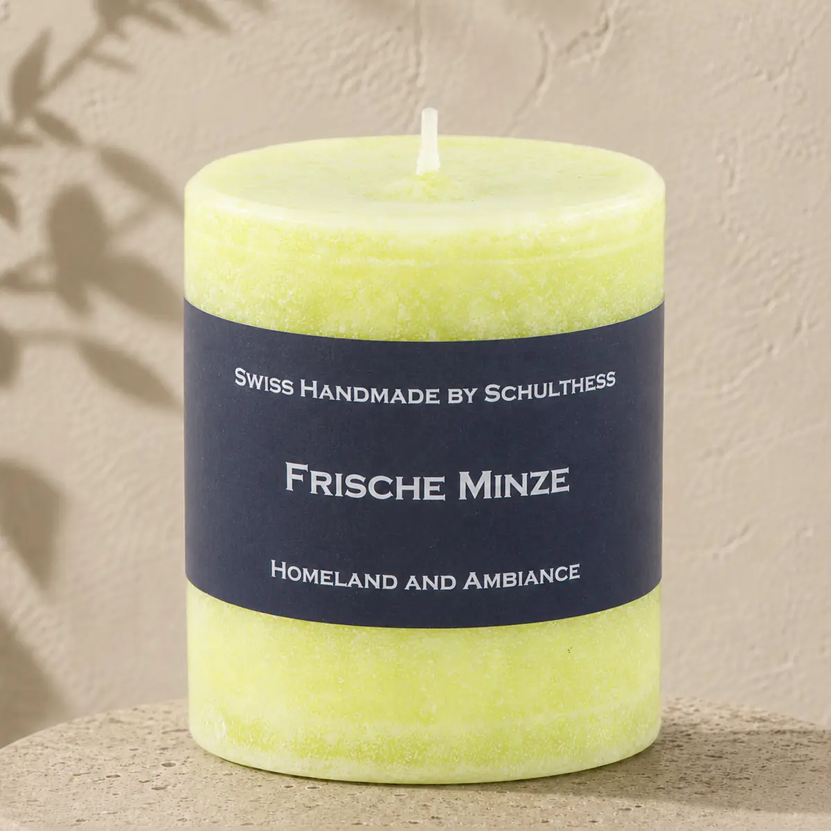Hellgrüne Schulthess Duftkerze Frische Minze auf einem runden Travertinsockel vor einer hellen, strukturierten Wand.
