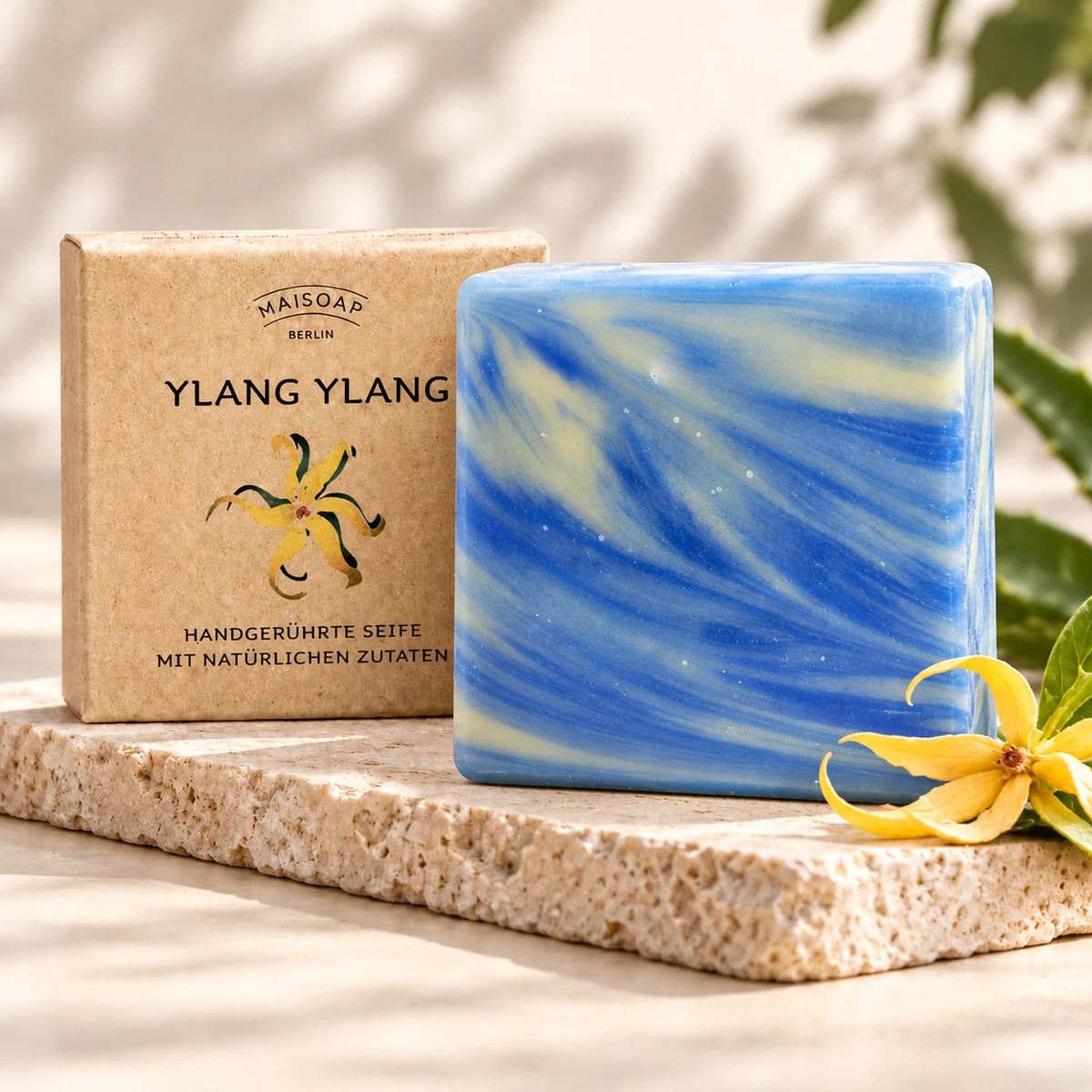 Blau-creme marmorierte Maisoap Ylang-Ylang-Seife mit Verpackung und gelber Blüte auf Steinplatte