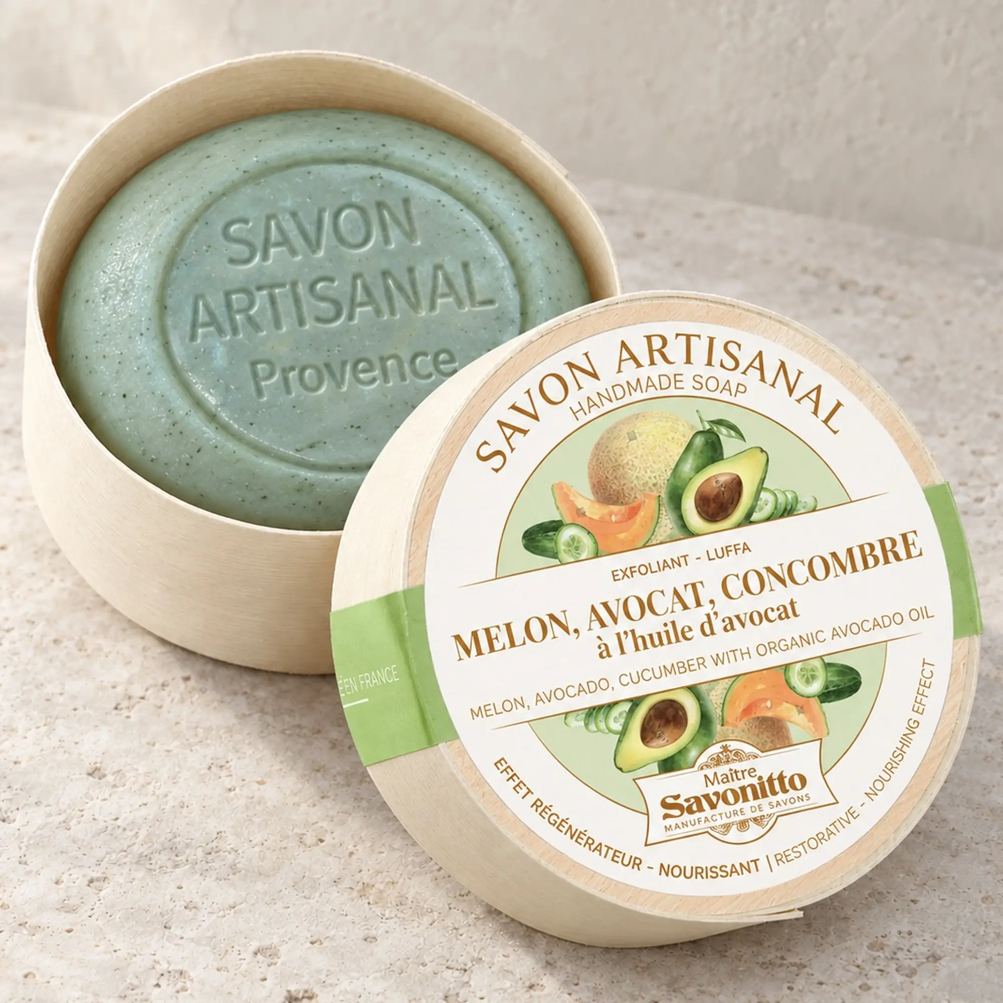 Maître Savonitto Melone, Avocado und Gurke in offener runder Holzschachtel mit angelehntem Etikettdeckel auf heller Steinfläche.