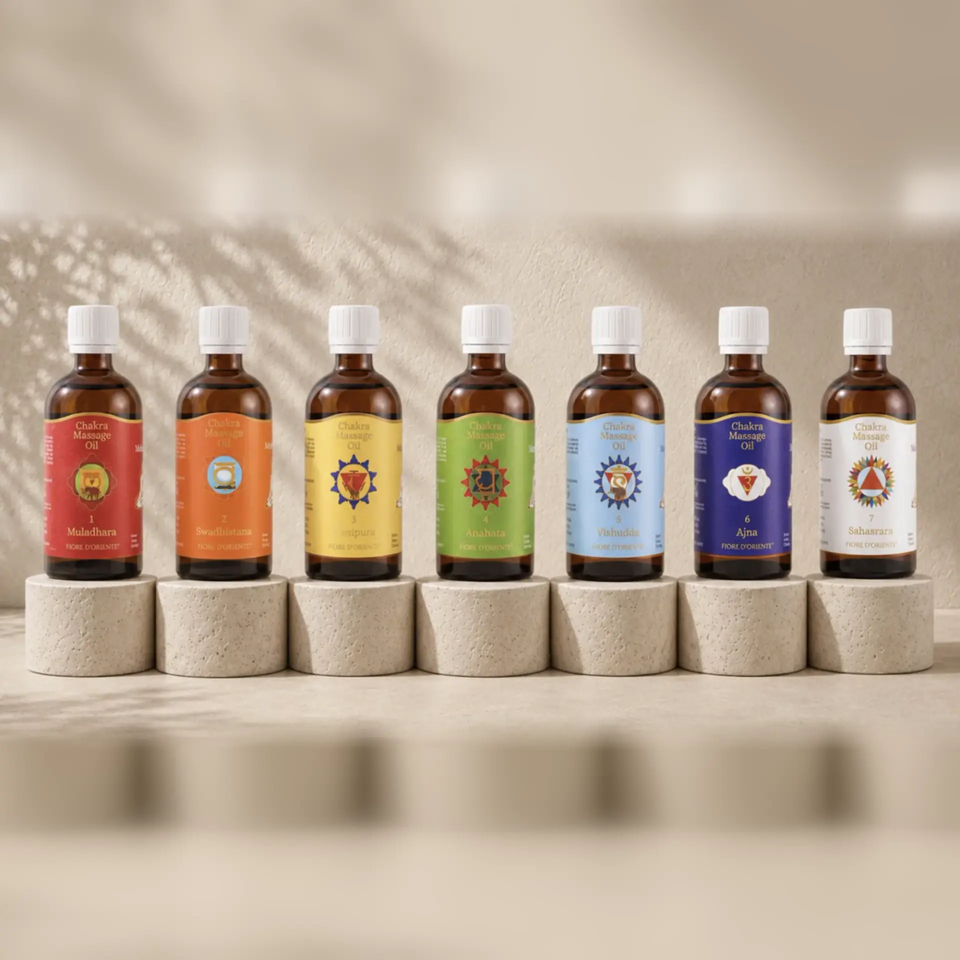 Sieben Chakra-Massageöle in den Farben der sieben Chakren auf hellen Travertinsockeln.