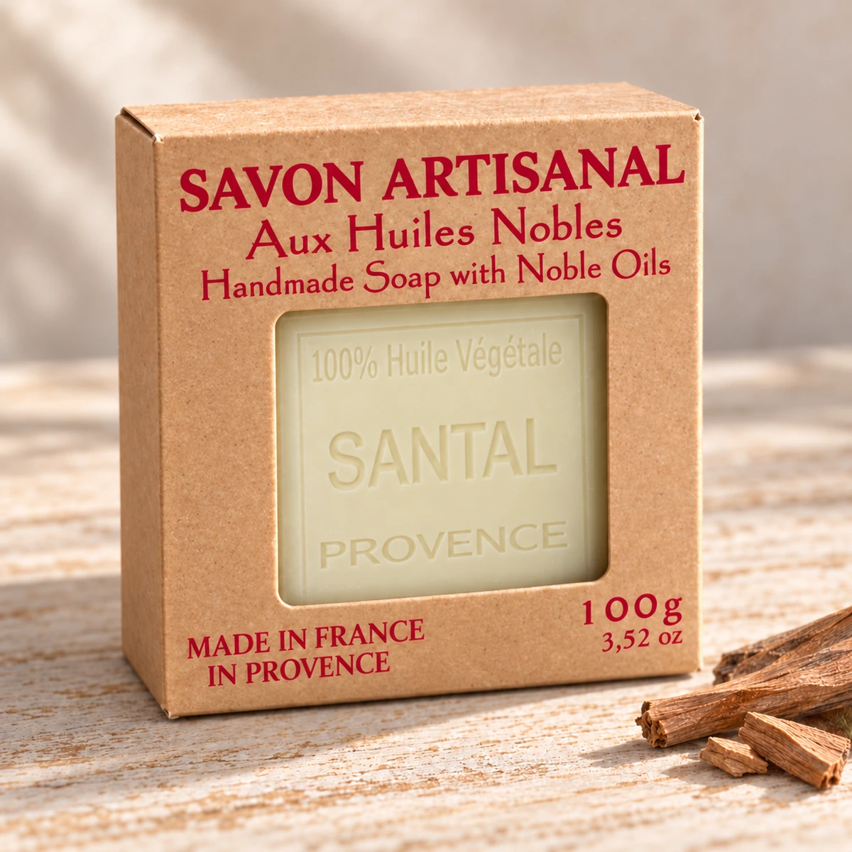 Maître Savonitto Seife Sandelholz in vollständig sichtbarer Kraftkartonverpackung mit Sichtfenster, neben Holzstücken und einem grünen Zweig auf hellem Holz.