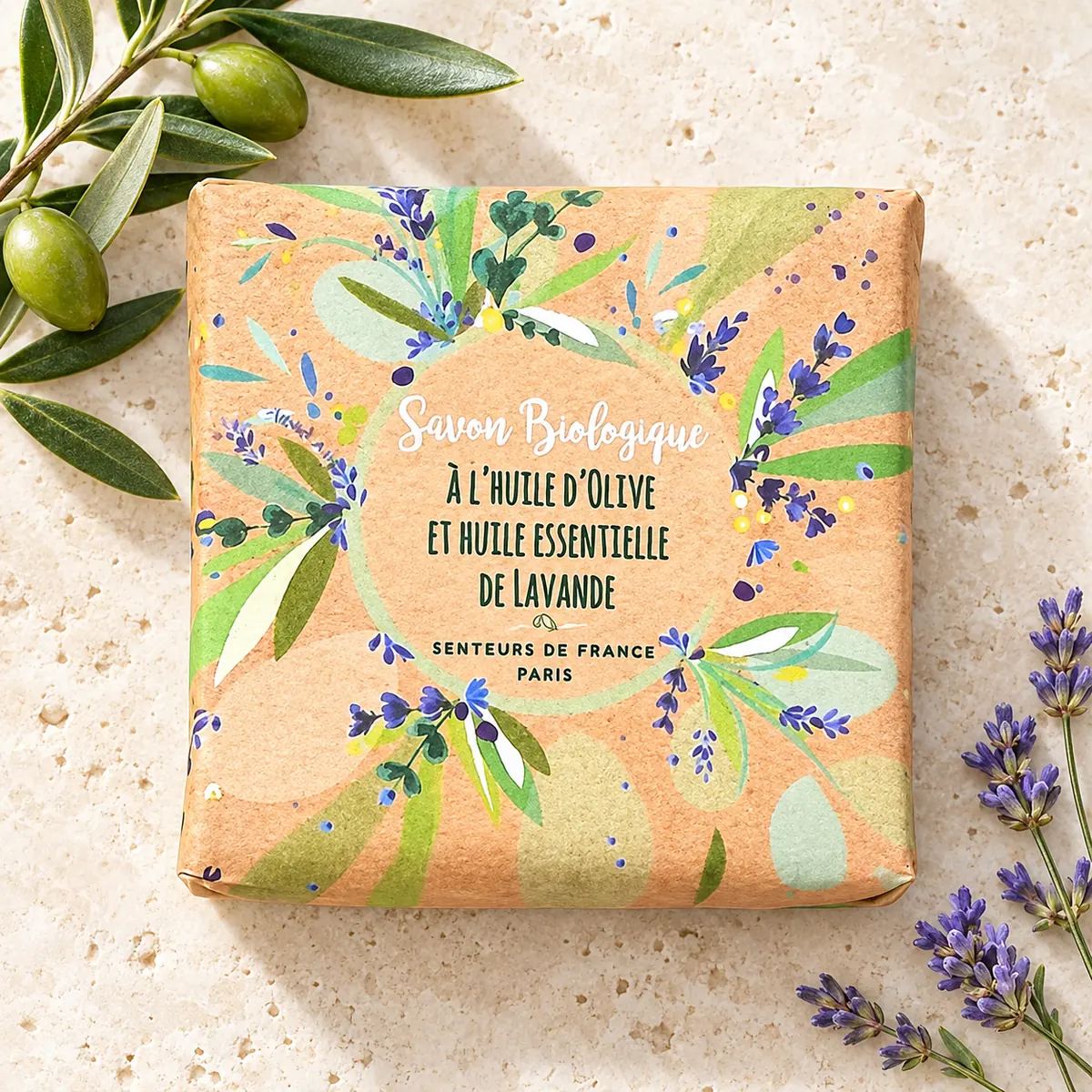 Verpackte Senteurs de France Bioseife mit Olivenöl und Lavendel, dekoriert mit Olivenzweig und Lavendel auf Travertin.